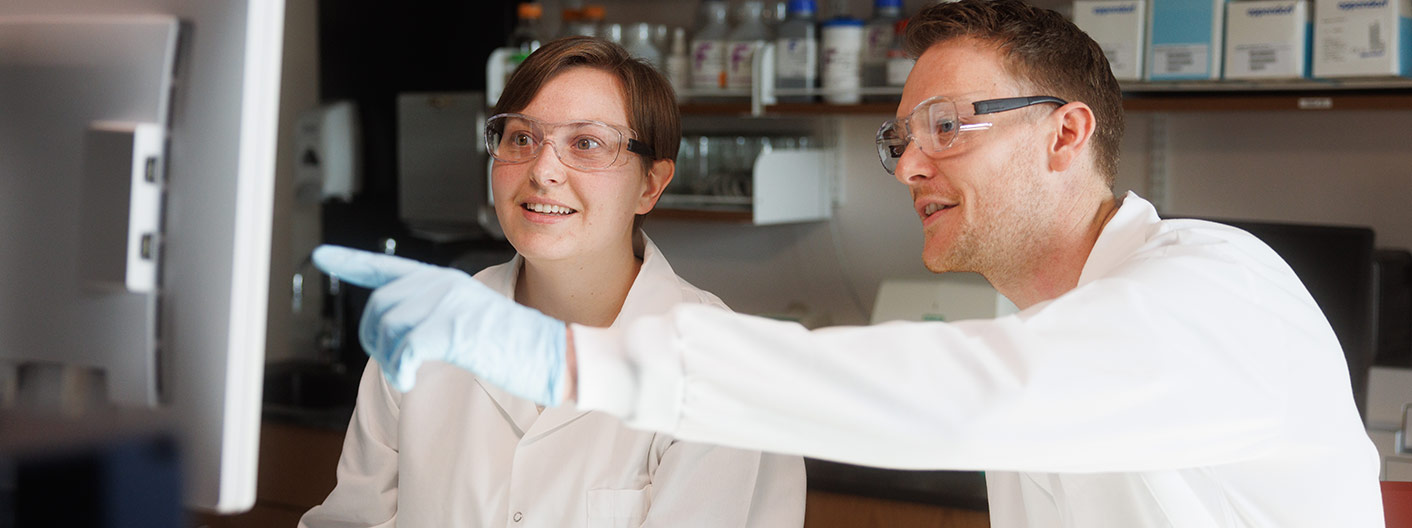 two people in PPE examine computer screen